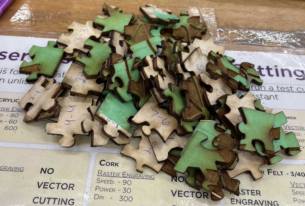 Pile of puzzle pieces with the excess painter's tape still attached. The backs of some of the pieces are visible and have their location written on the back in pen (i.e. 7-6 for it being in the 7th column, 6th row).