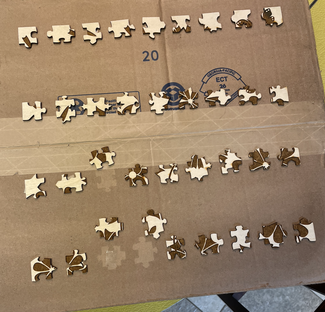 Four rows of puzzle pieces on top of a cardboard box. Three of the pieces have been moved to reveal piece-shaped outlines on the box.